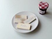 Three small wooden blocks with text on a white plate next to a jar of jam.