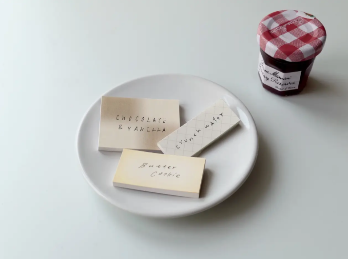 Three small wooden blocks with text on a white plate next to a jar of jam.