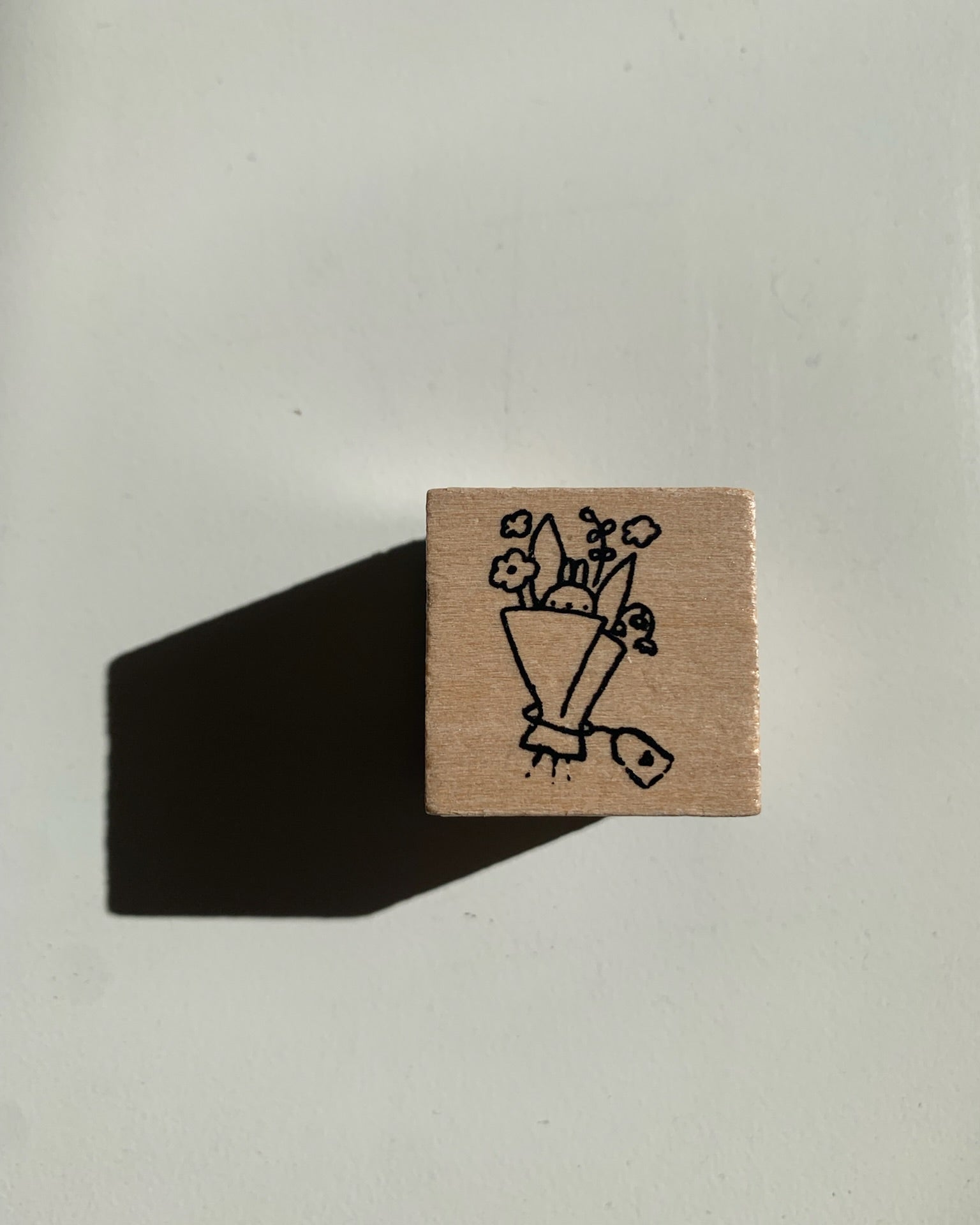 Small wooden stamp with a black illustration of flowers in a vase on a light gray background