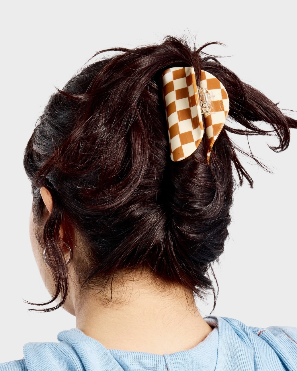 Person with a checkered hair clip in their hair against a light background