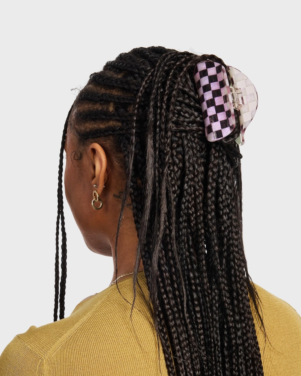 Person with braided hair wearing a checkered hair clip on a plain background