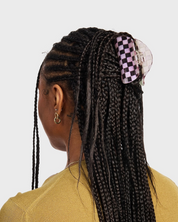 Person with braided hair wearing a checkered hair clip on a plain background