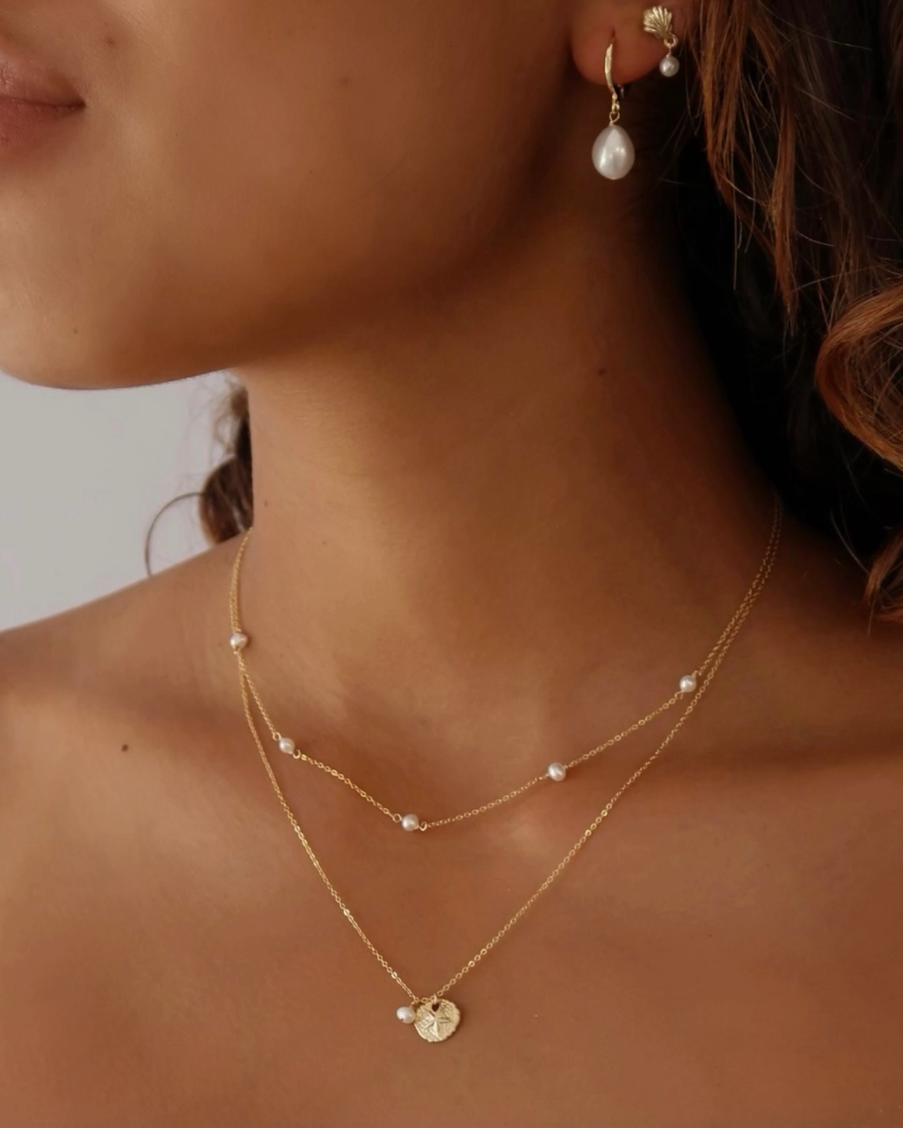 Close-up of a woman wearing a gold necklace and earrings with pearls.