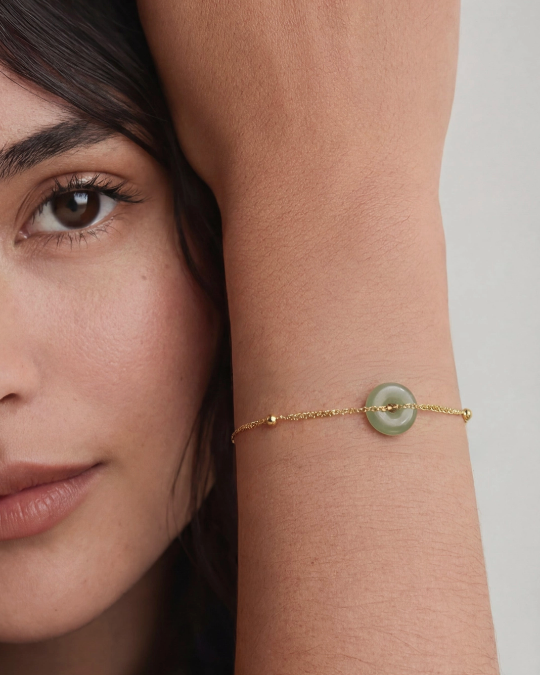 Woman wearing a gold bracelet with a green gemstone on a neutral background