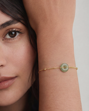 Woman wearing a gold bracelet with a green gemstone on a neutral background