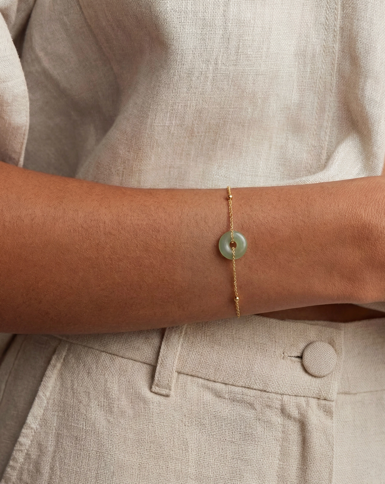 Close-up of a person's arm wearing a gold bracelet with a green stone on a neutral background.