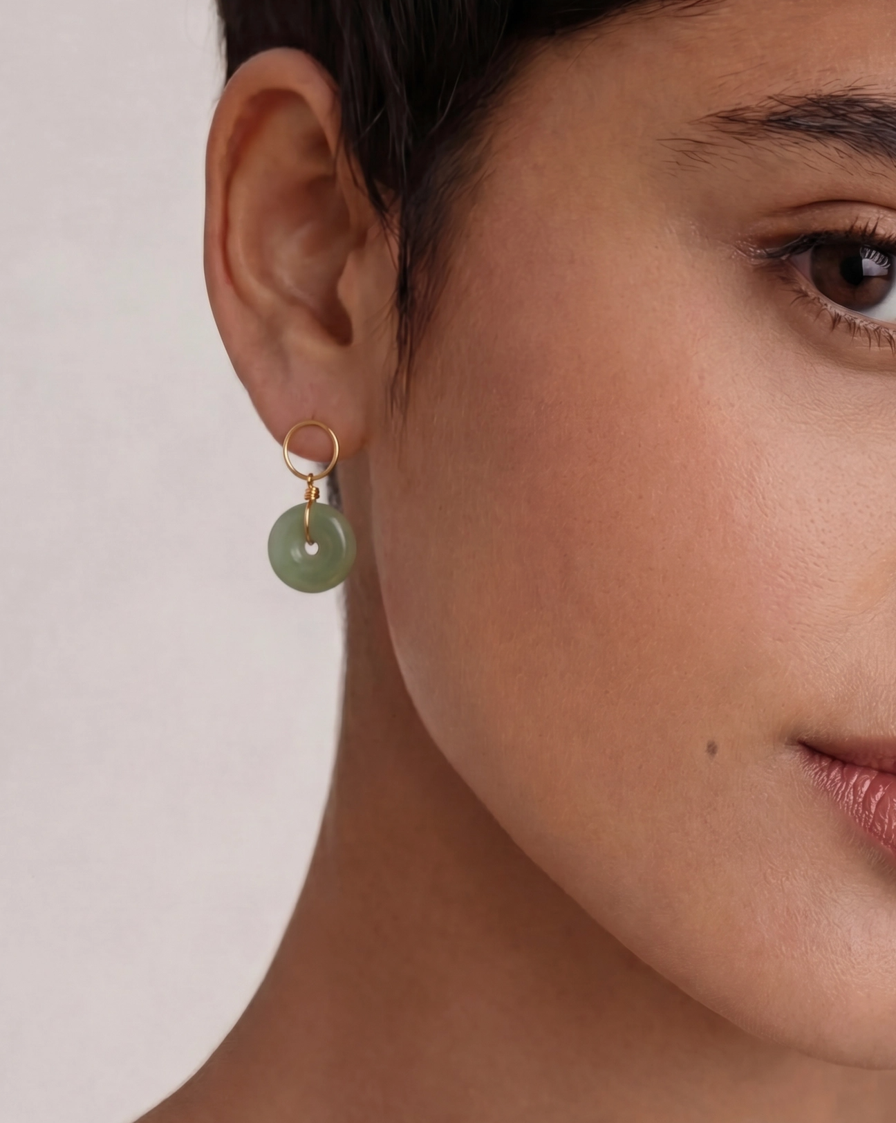 Close-up of a person wearing a green earring with a plain background