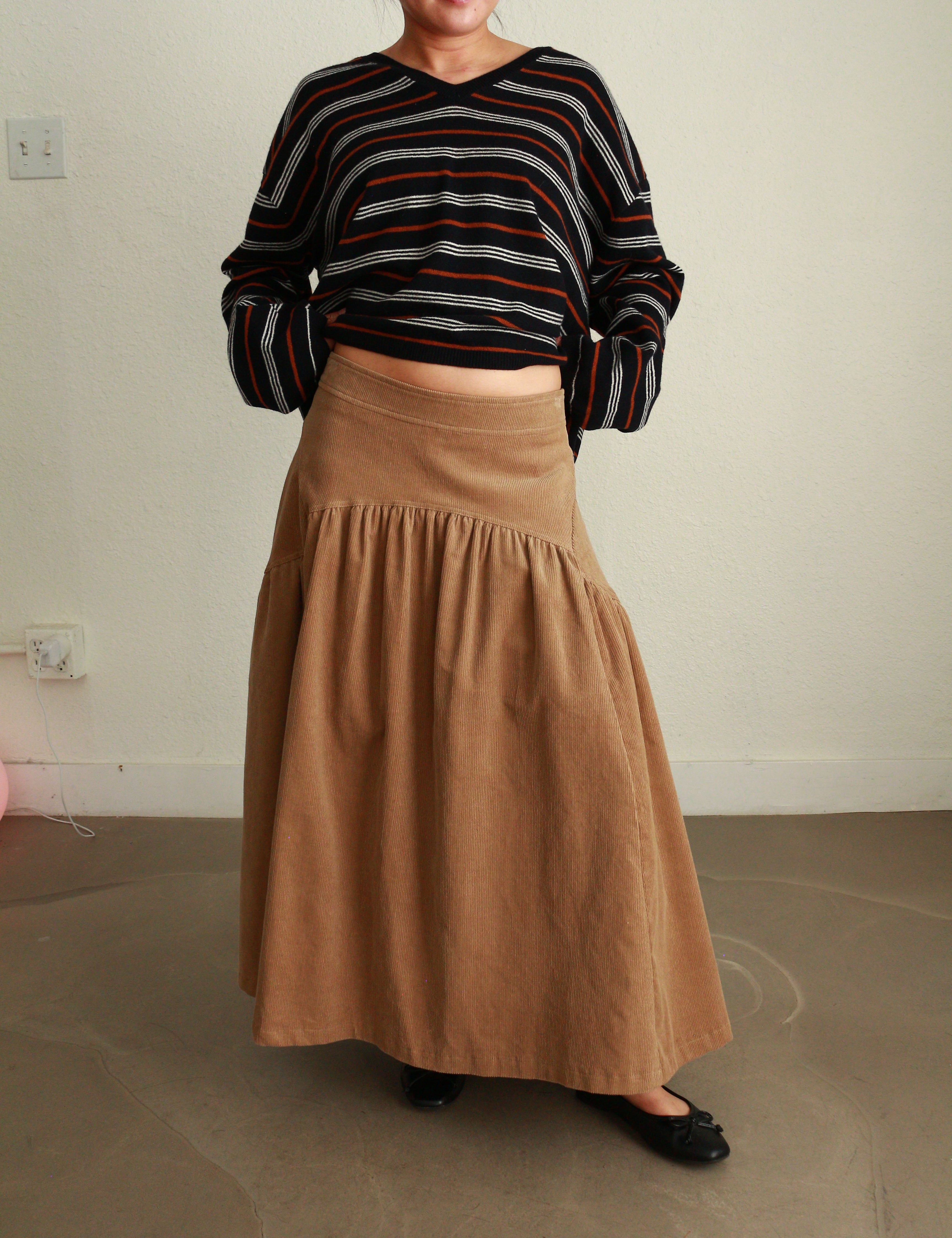 Person wearing a striped shirt and brown skirt in a minimal indoor setting