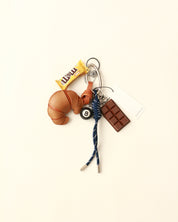 Keychain with croissant, chocolate bar, and bell on a beige background