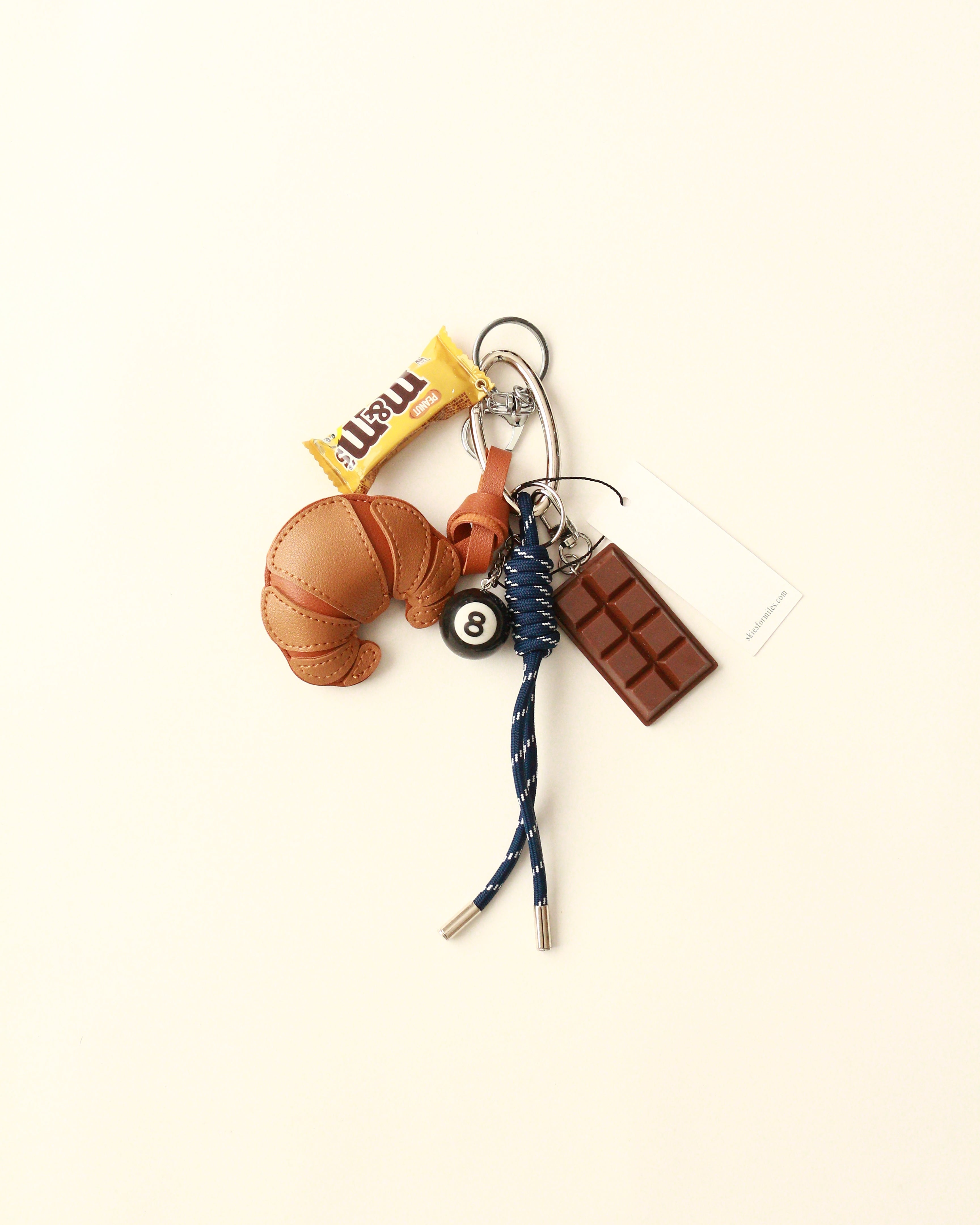 Keychain with croissant, chocolate bar, and bell on a beige background