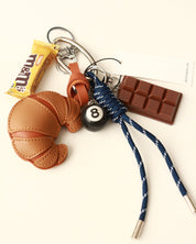 Keychain with various charms including a croissant, candy bar, and number 8 ball on a white background.