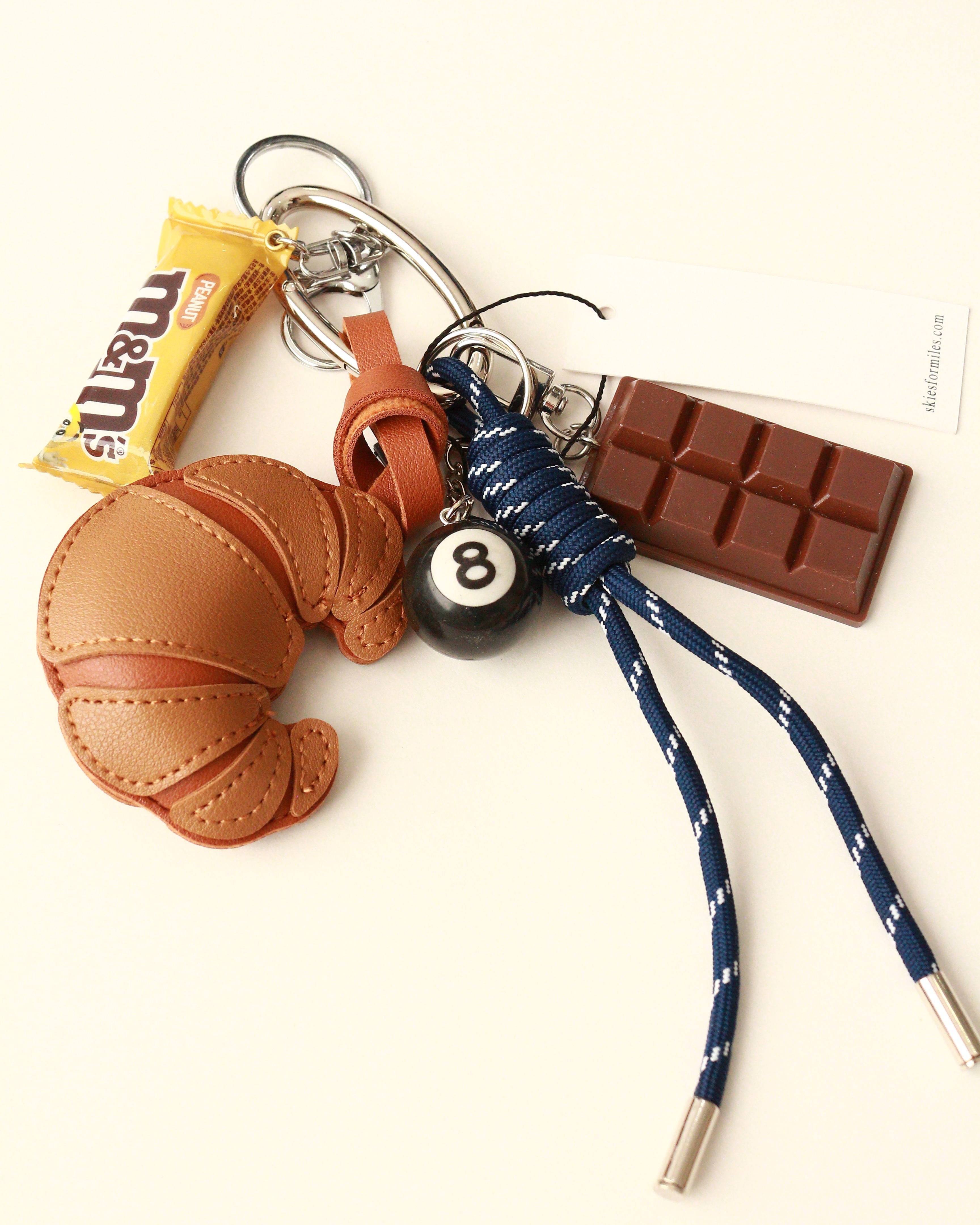 Keychain with various charms including a croissant, candy bar, and number 8 ball on a white background.
