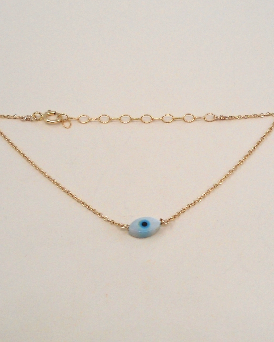 Gold bracelet with a blue eye charm on a beige background