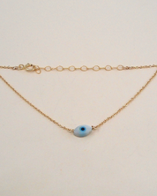 Gold bracelet with a blue eye charm on a beige background