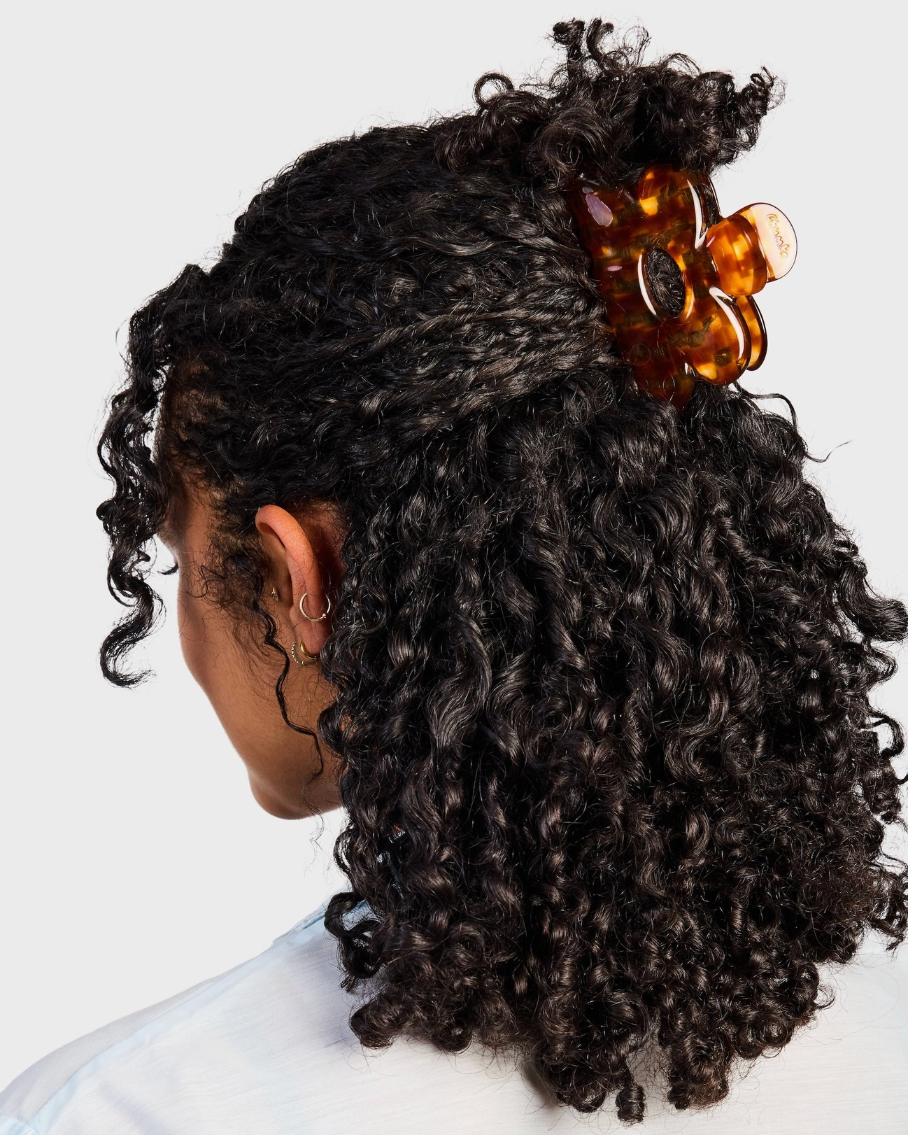 Person with curly hair wearing a tortoiseshell barrette on a white background