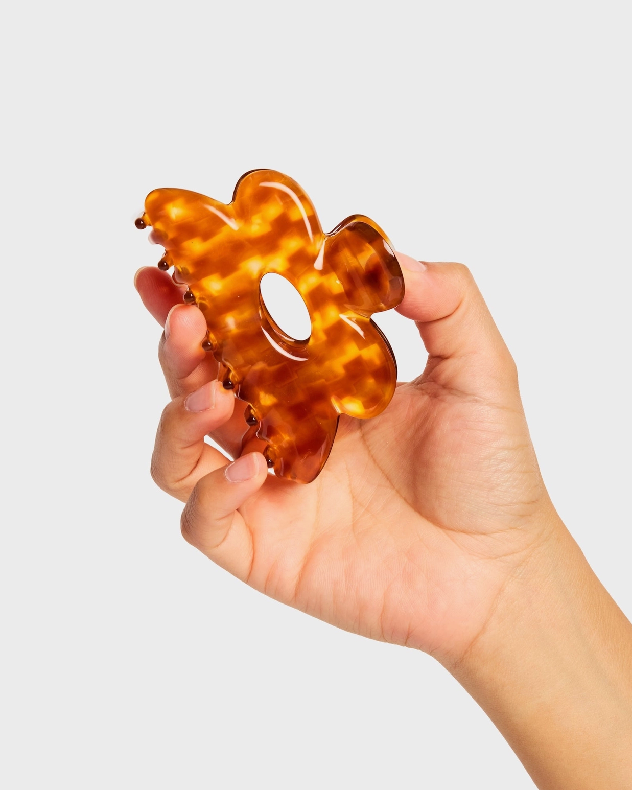 Hand holding a tortoiseshell patterned hair clip against a light gray background