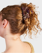 Woman with curly hair tied back with a decorative scrunchie on a plain background