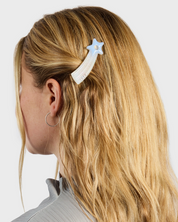 Person with blonde hair wearing a star-shaped hair clip on a plain background