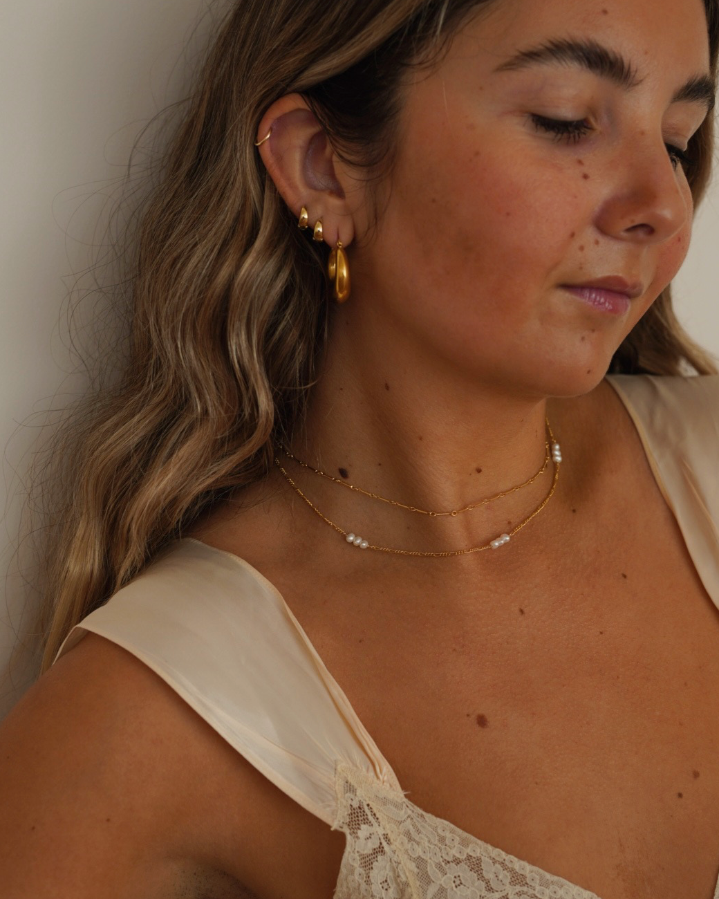 Woman wearing gold earrings and a delicate necklace against a neutral background