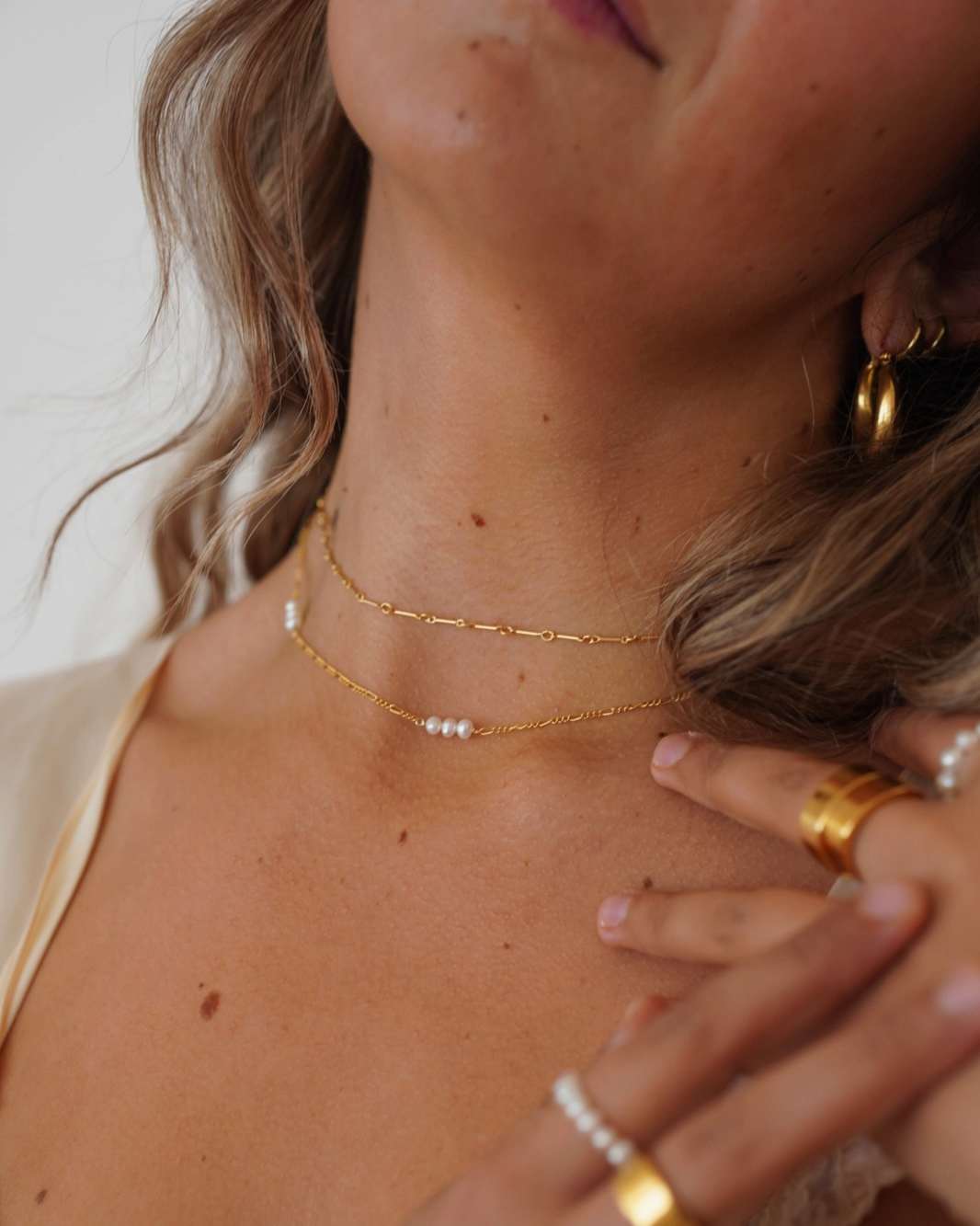 Close-up of a person wearing gold jewelry including necklaces, rings, and earrings.
