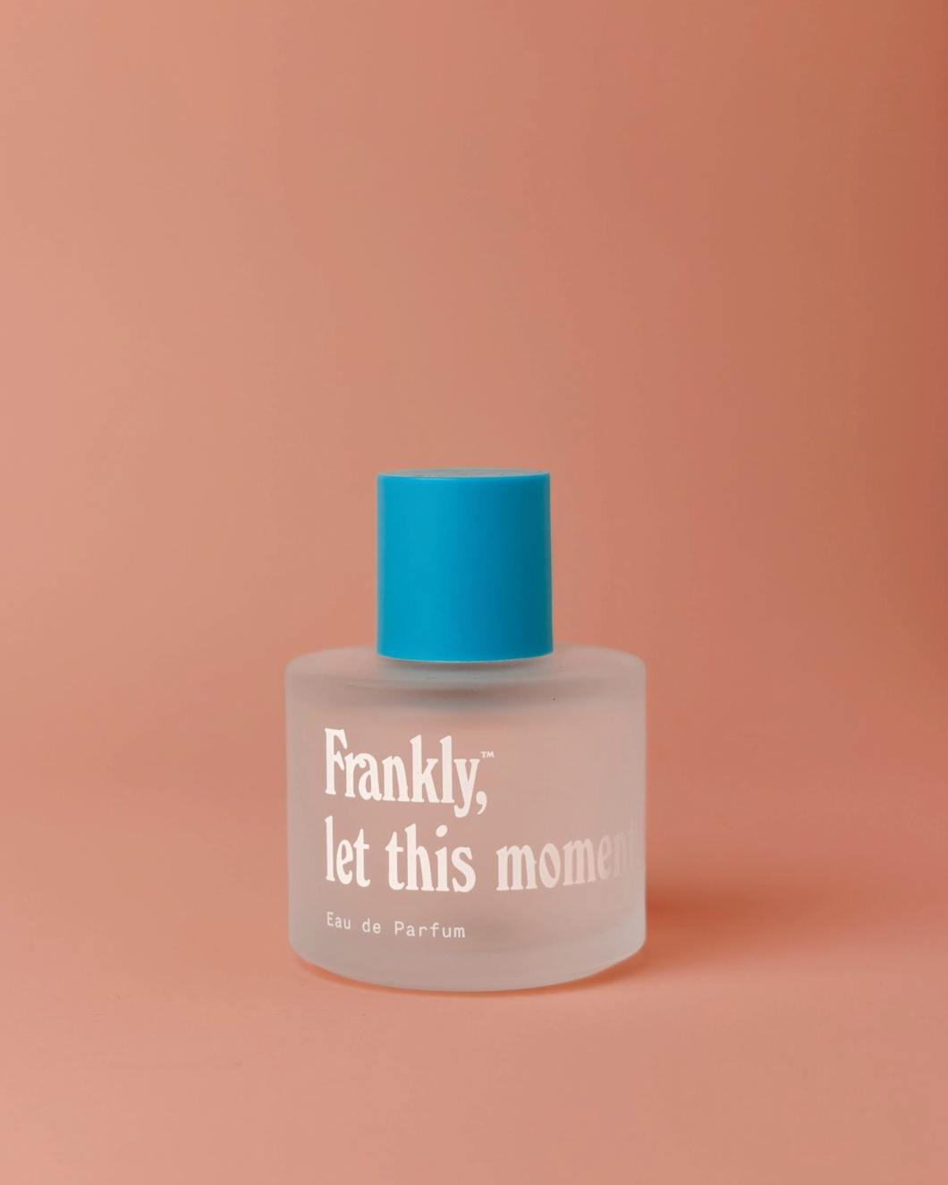 Perfume bottle with blue cap and clear body on a peach background