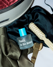 Perfume bottle labeled 'Frankly, let this moment' with a brush and fabric on a white background