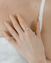 Close-up of a hand wearing a silver ring with a unique design on a neutral background