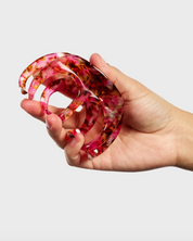Hand holding a pink and red marbled hair clip against a light gray background