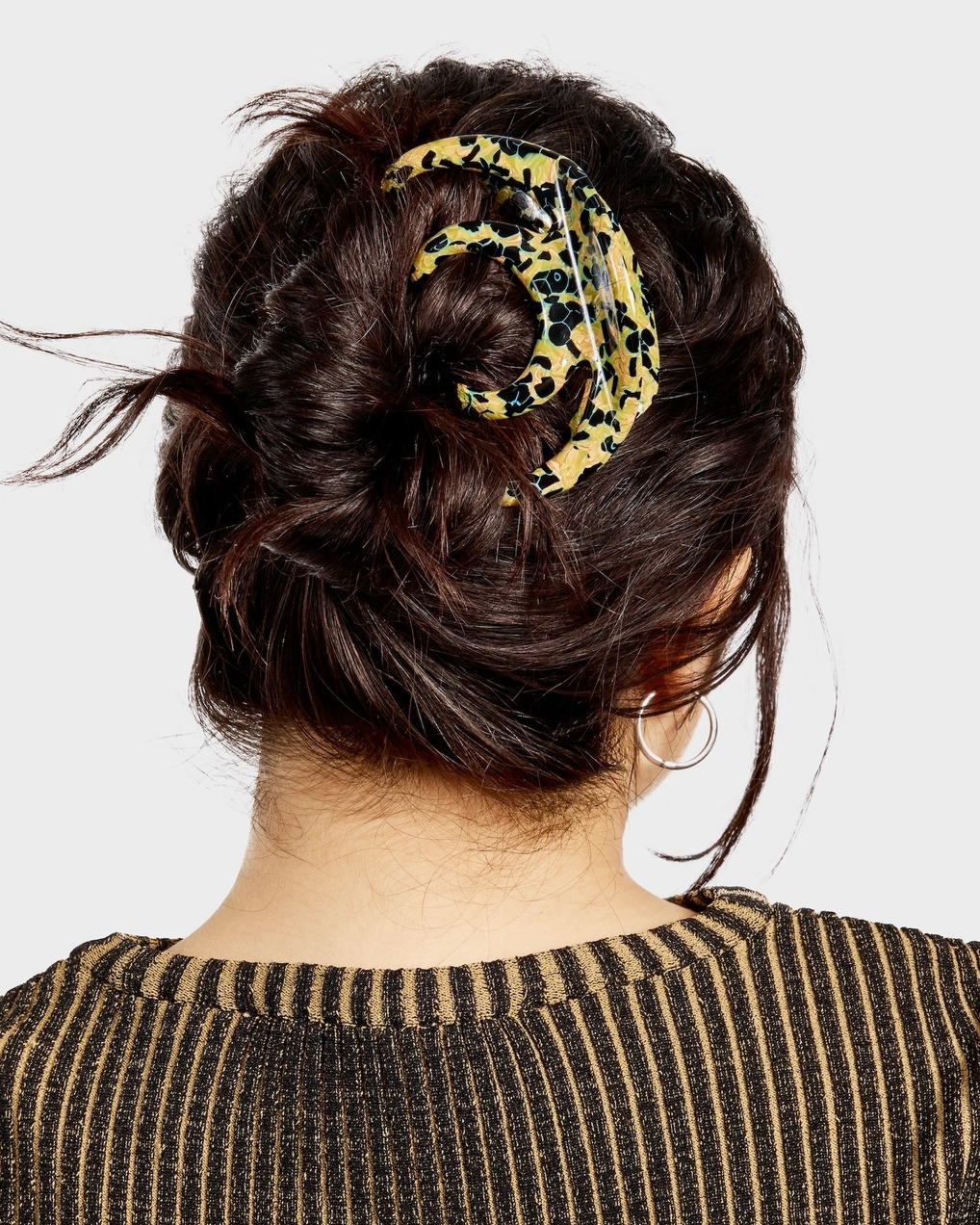 Person with a stylish hair bun adorned with a leopard print scarf on a plain background