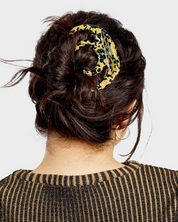 Person with a stylish hair bun adorned with a leopard print scarf on a plain background