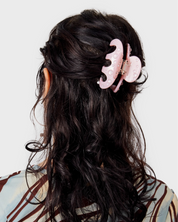 Person with long dark hair wearing a pink hair clip on a light gray background