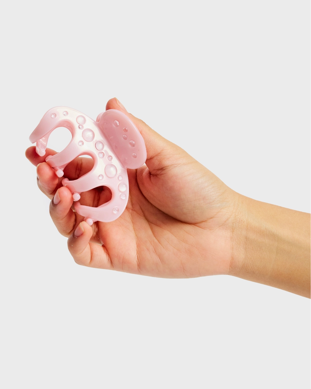 Hand holding a pink silicone baby teether against a light gray background