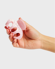 Hand holding a pink silicone baby teether against a light gray background