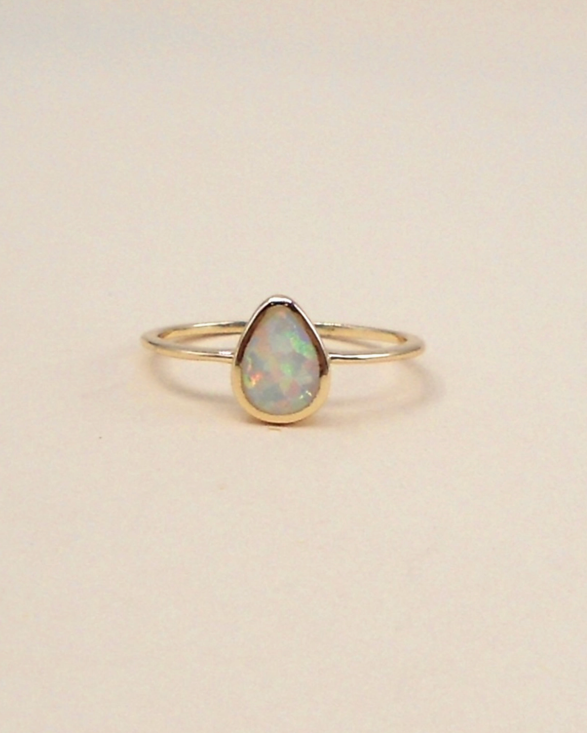 Gold ring with a teardrop-shaped opal stone on a beige background