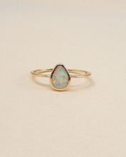 Gold ring with a teardrop-shaped opal stone on a beige background