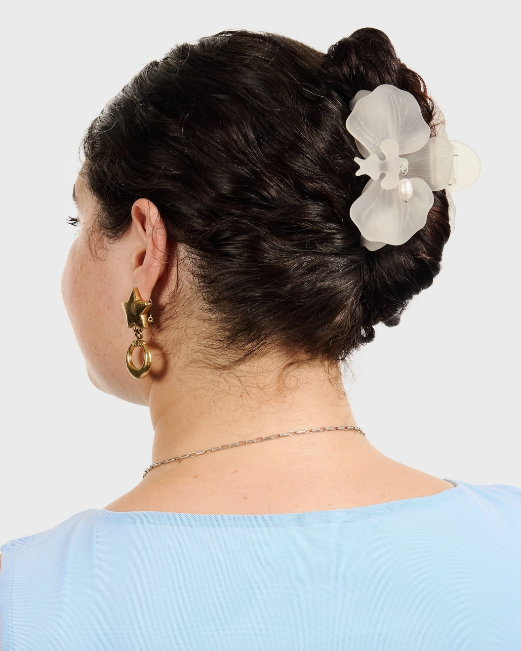 Woman with styled hair featuring a white flower hair claw clip against a plain background