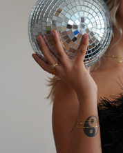 Hand holding a disco ball with a tattoo on the arm against a neutral background