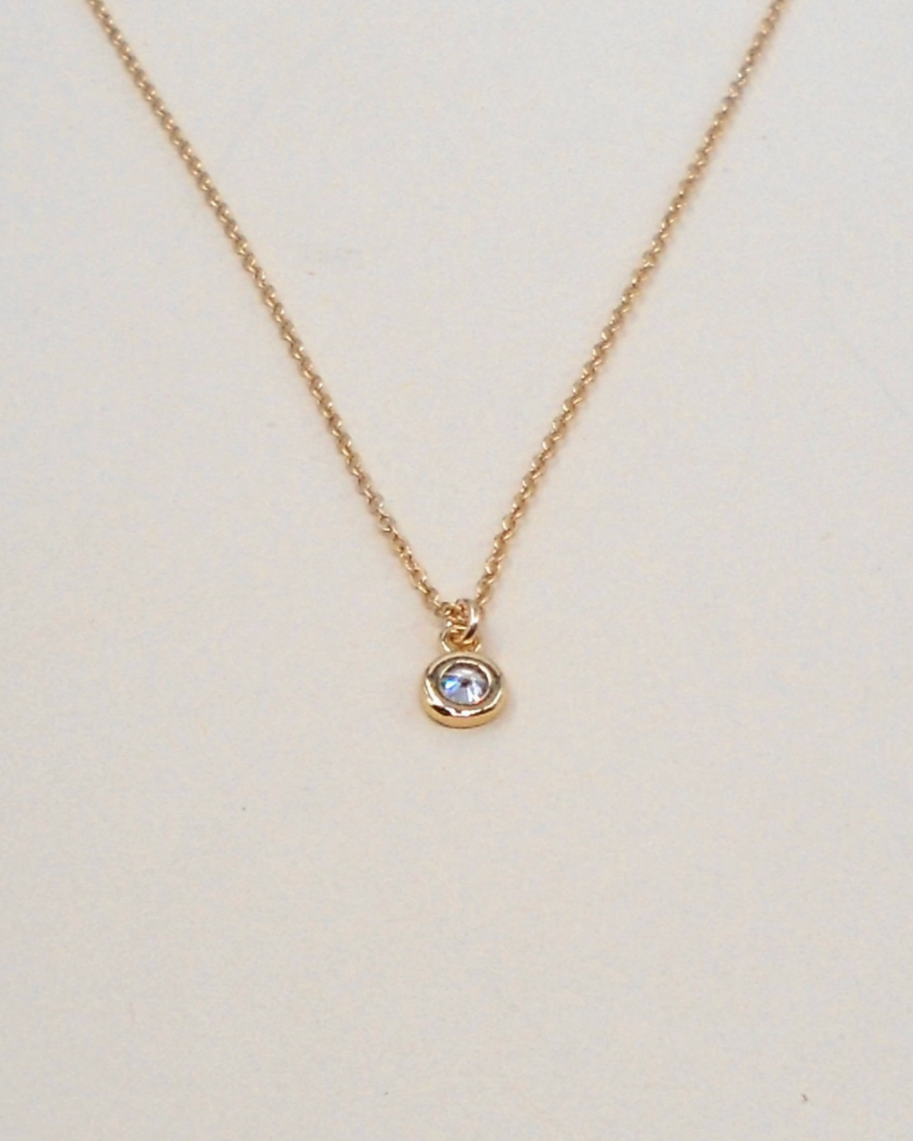 Gold necklace with a small round pendant on a light beige background