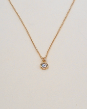 Gold necklace with a small round pendant on a light beige background