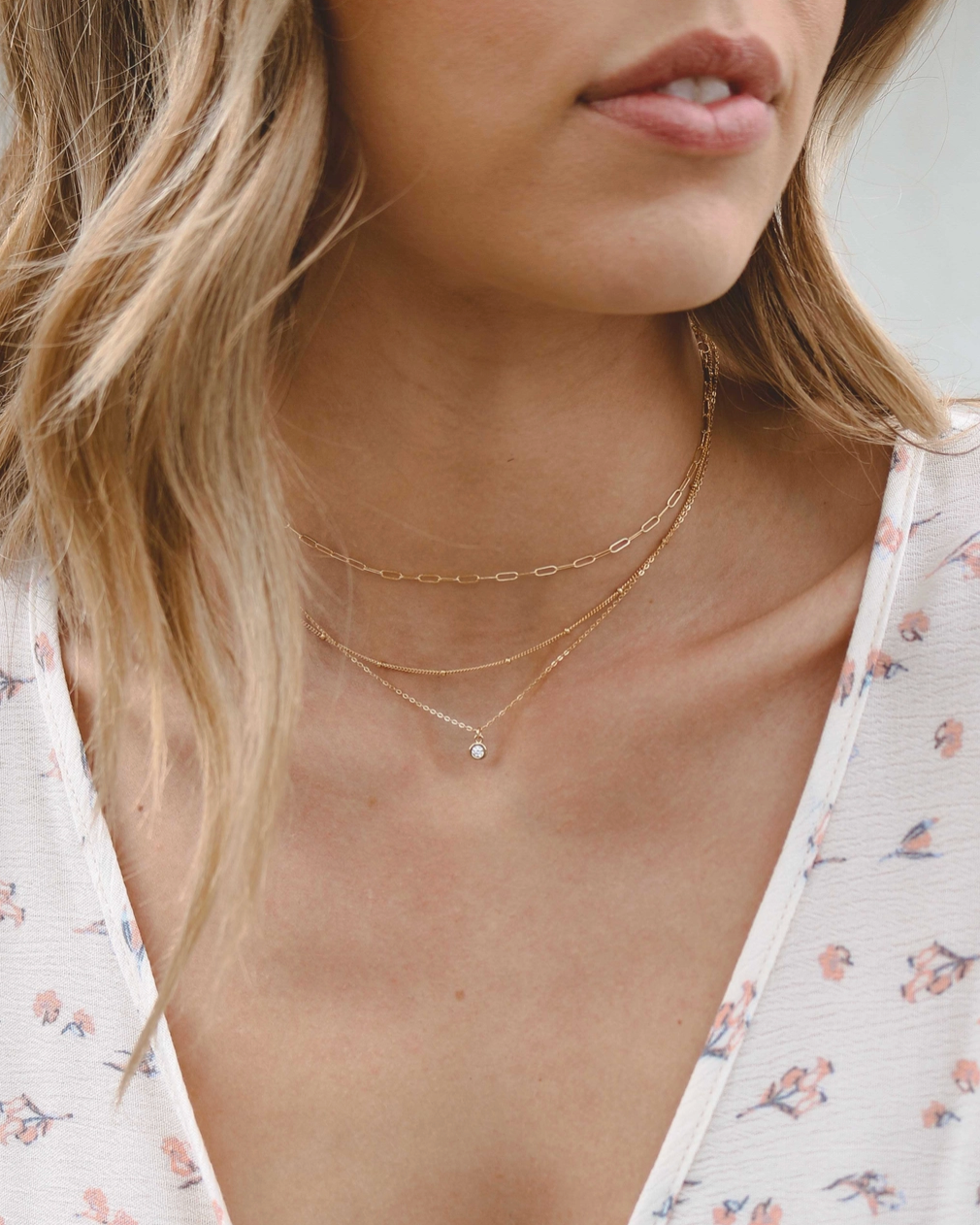 Close-up of a woman wearing a delicate gold necklace with a floral blouse.