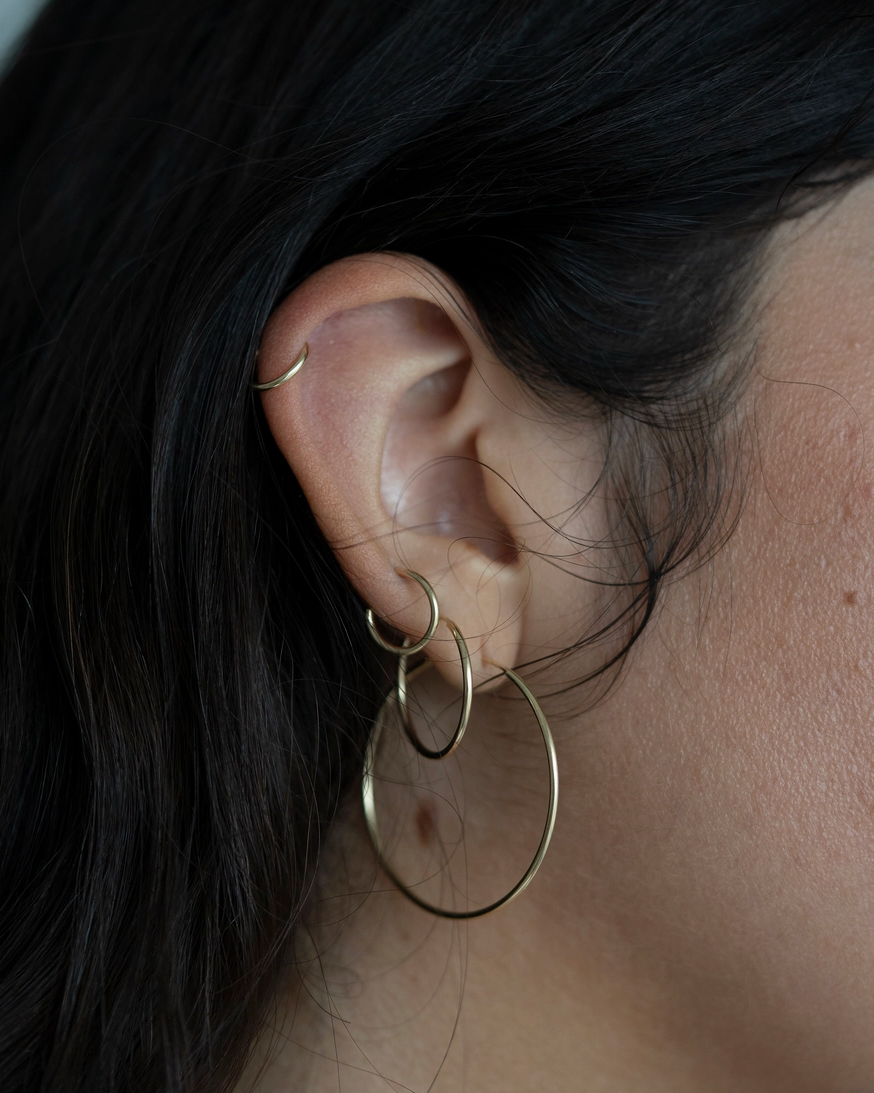 Close-up of an ear wearing a gold hoop earring with dark hair and skin in the background