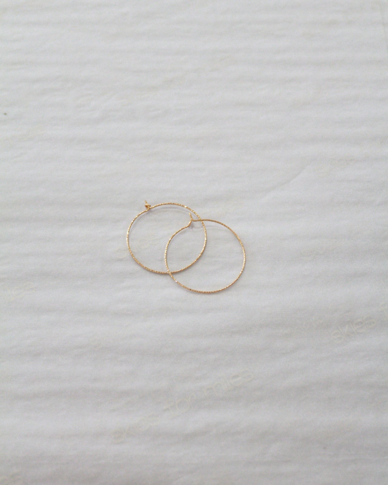 Two thin gold hoop earrings resting on a textured white fabric background.