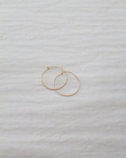 Two thin gold hoop earrings resting on a textured white fabric background.