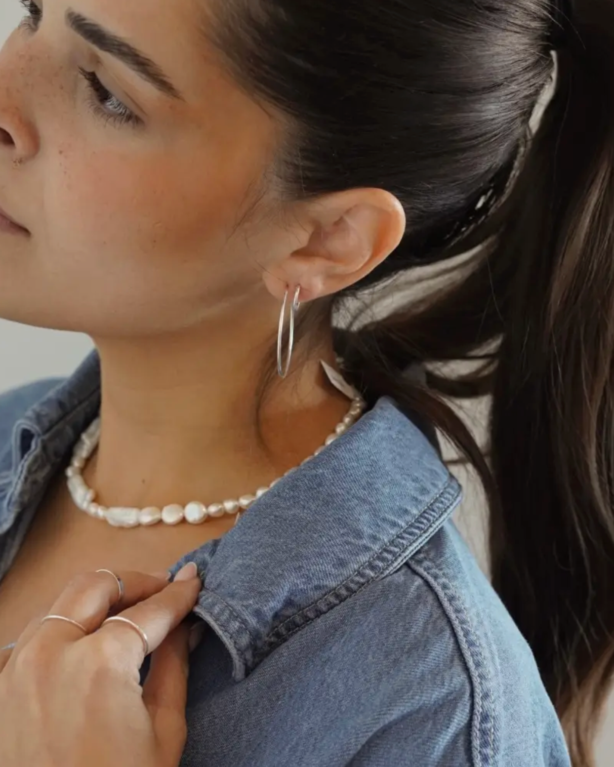 Woman wearing a pearl necklace and hoop earrings, with a blurred background