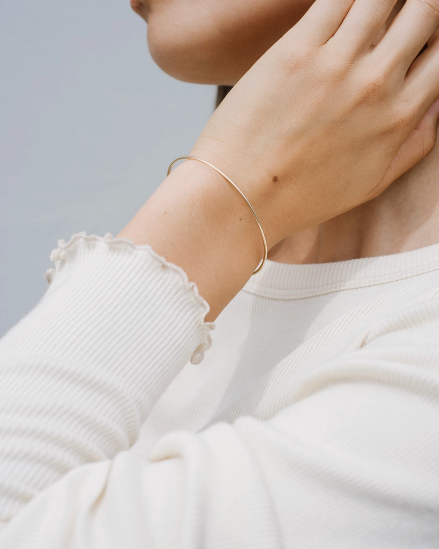 Person wearing a gold bracelet on a neutral background