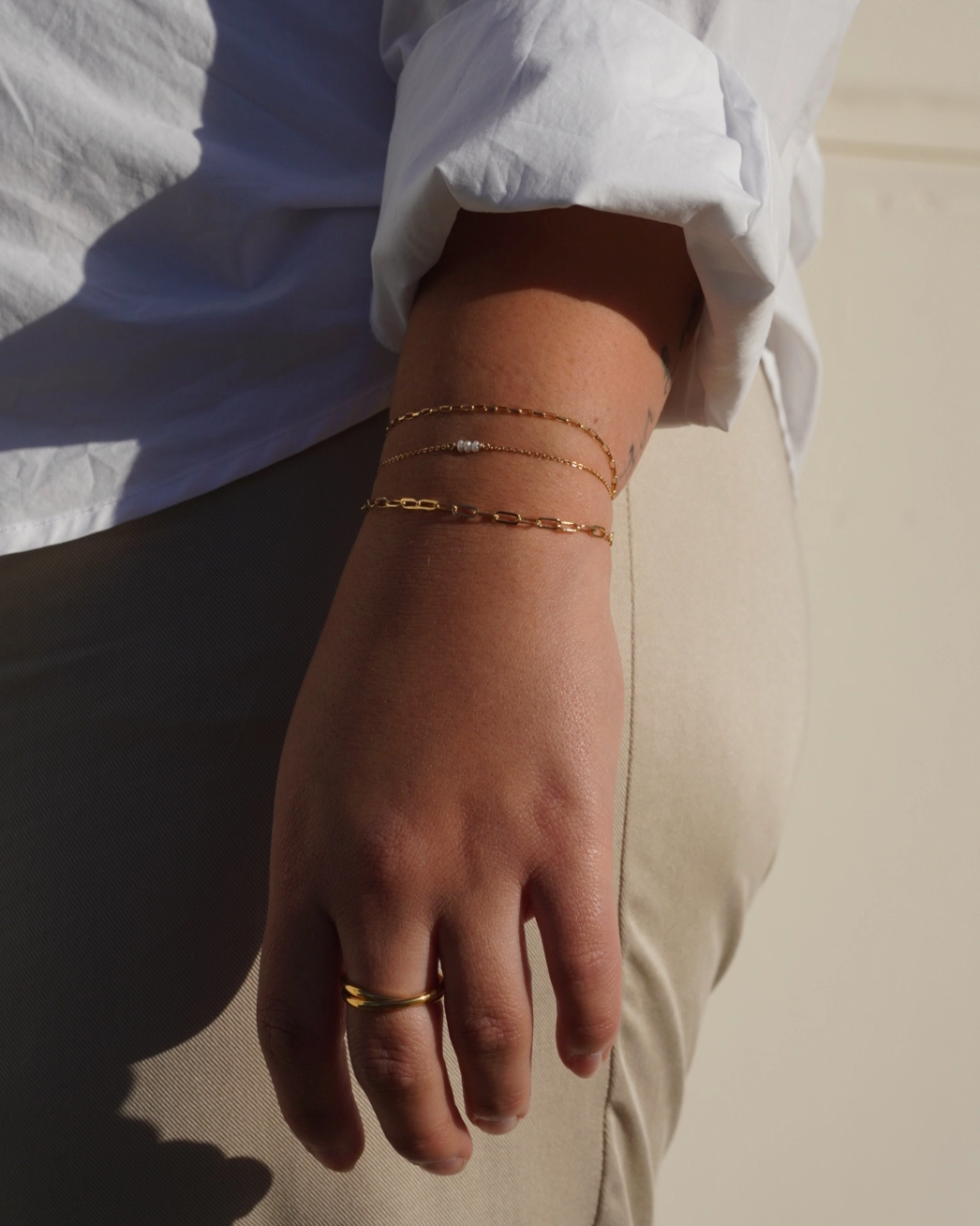 Close-up of a person's wrist with gold bracelets and a ring, wearing a white shirt.