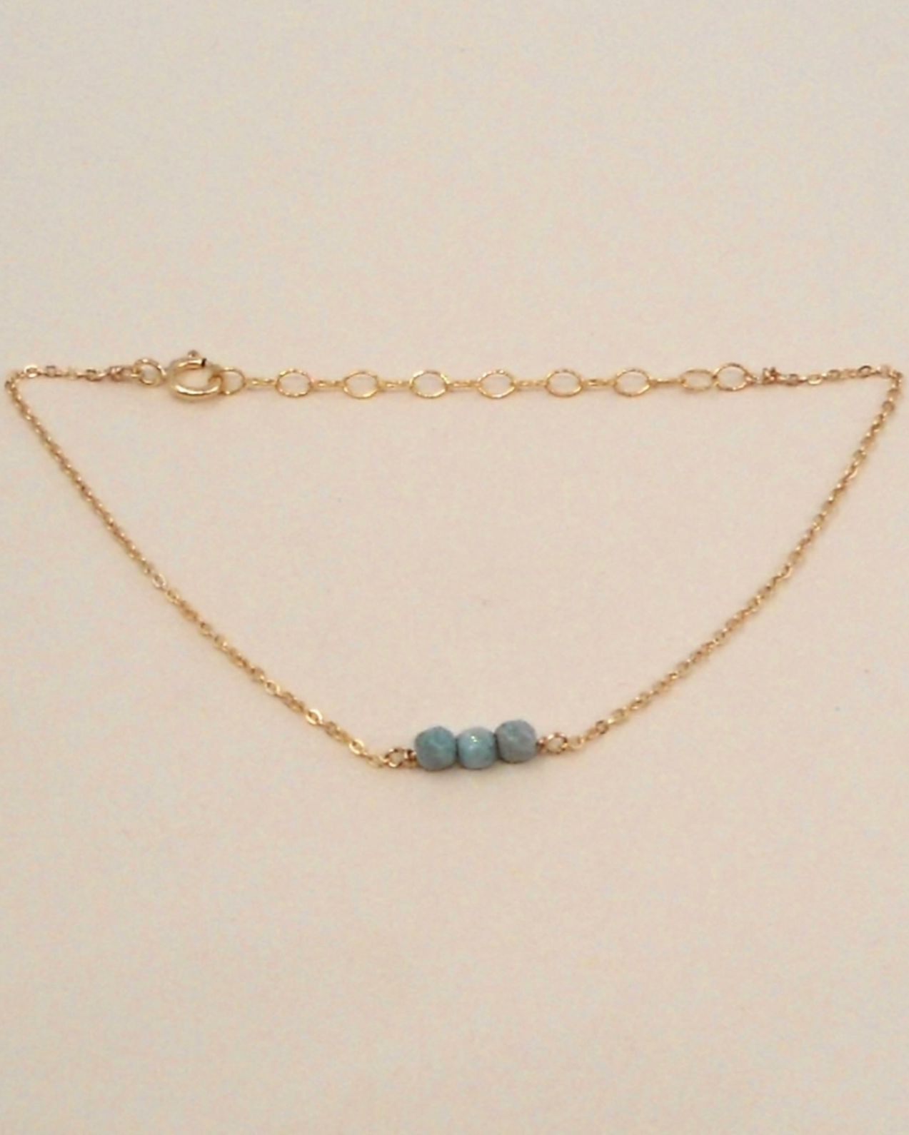 Gold bracelet with three blue beads on a beige background