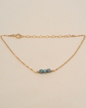 Gold bracelet with three blue beads on a beige background