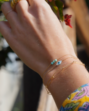 Close-up of a hand wearing gold bracelets with a blurred natural background