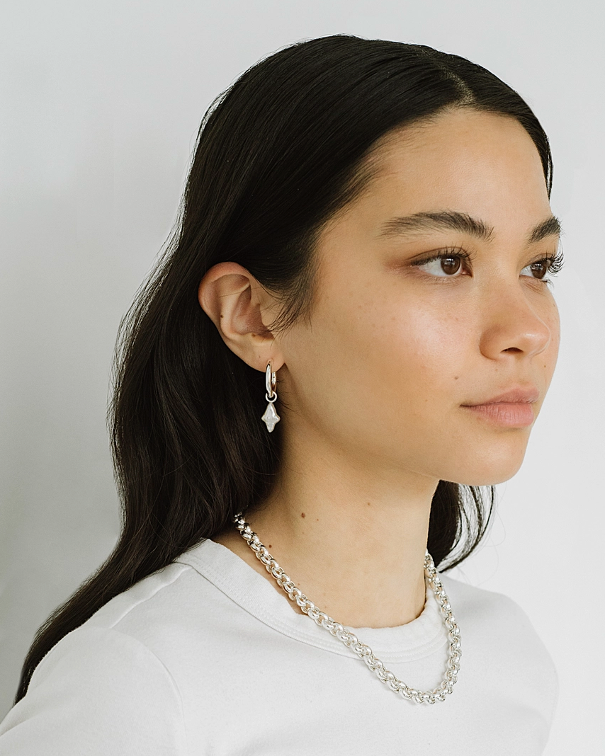 Woman wearing a white top and pearl necklace against a plain background